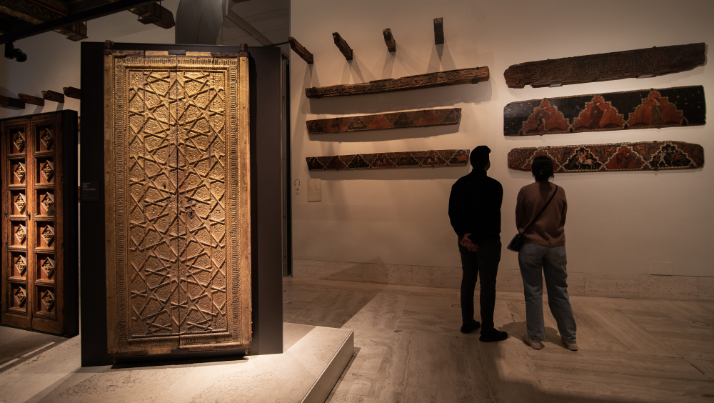 Museum room with visitors looking at decorated wood pieces
