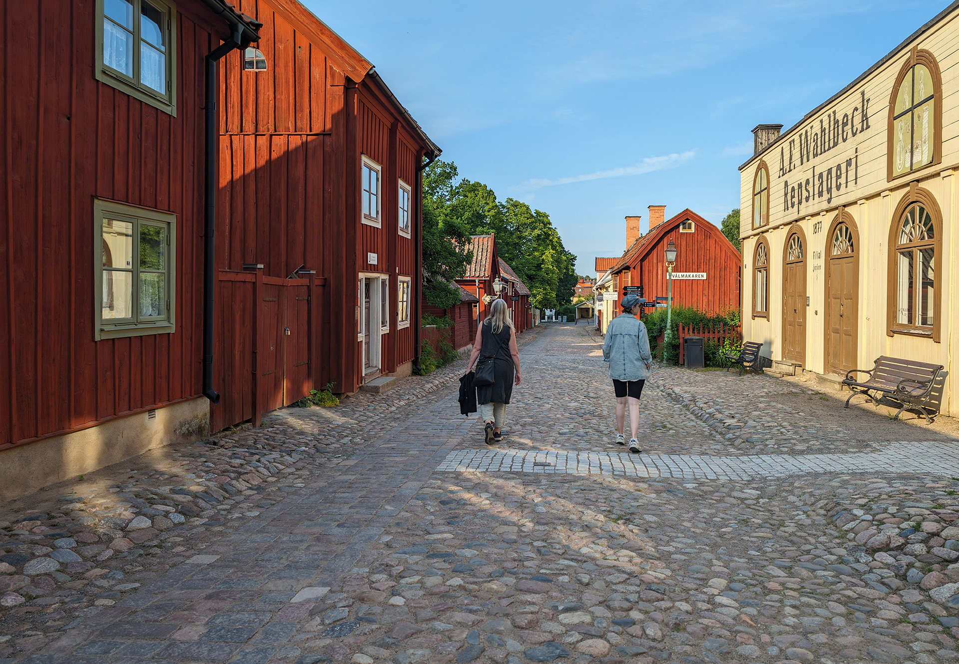 Two ladies are walking in the old quarter on a wide cobblestone street surrounded by older wooden buildings.