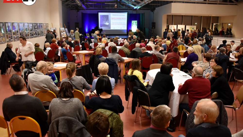 The event promoting the book candles was put out by the war. A lot of people sitting on chairs in front of the stage and a large screen on which the history of the book's creation is presented.