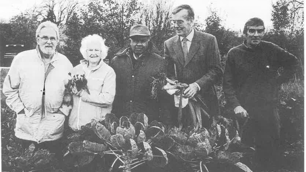Five people standing in an allotment, holding up leeks and brussel sprouts