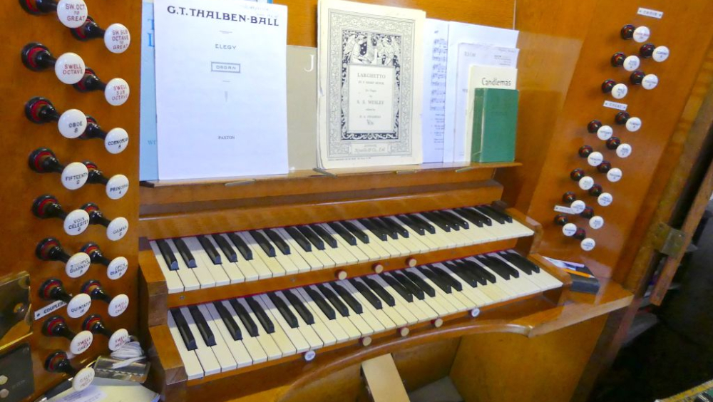 Close up view of an organ console, with keyboard and buttons, with music laid out ready to play.