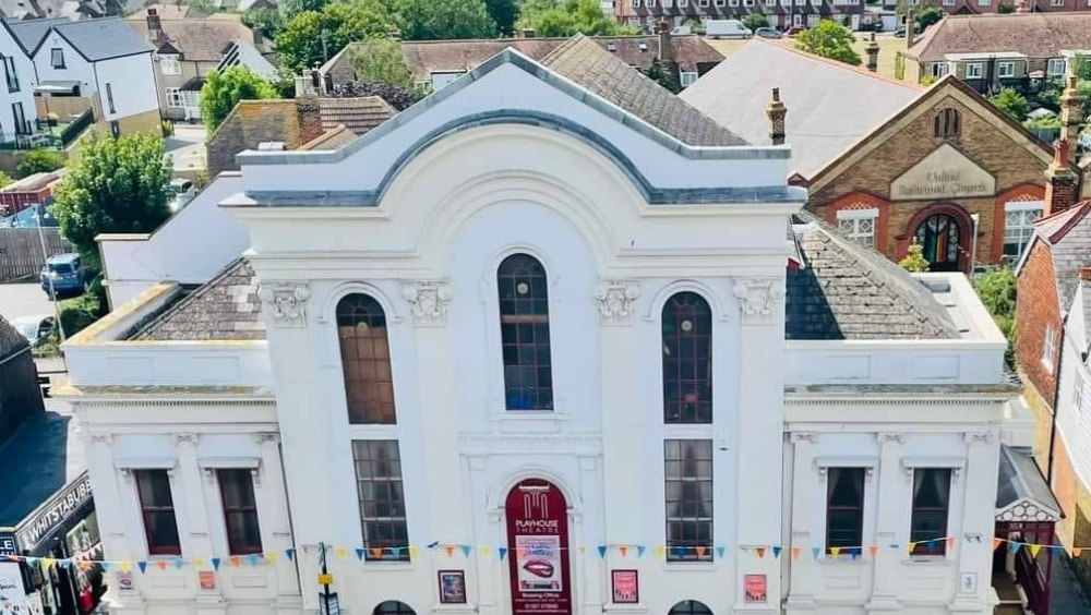 Aerial view of the front of an imposing white building with three narrow arched windows at the centre. The town recedes into the background around and beyond the building.
