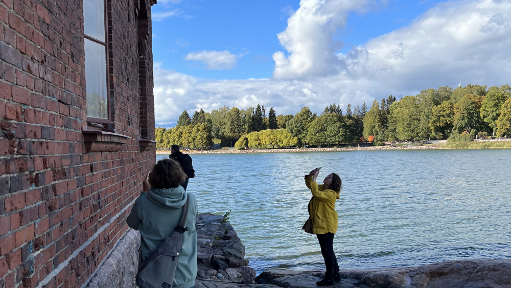 People are standing next to the building's beside the water and they are taking photos.