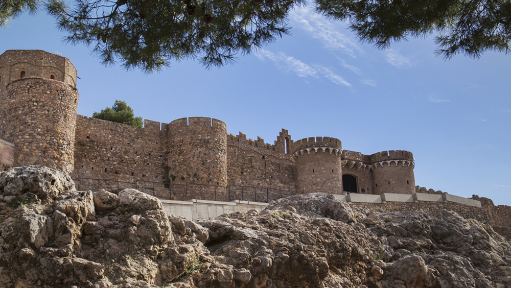 "Majestic view of Onda Castle, framed by rocky terrain and tree branches, showcasing its medieval stone walls and fortified entrance."