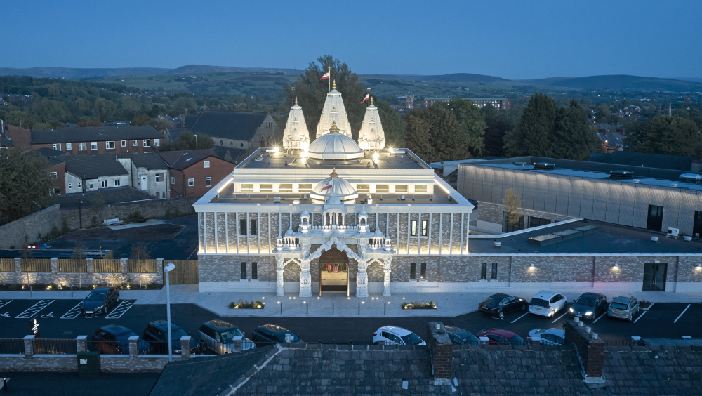 The main entrance of Shree Swaminarayan Mandir Oldham lit up at night.