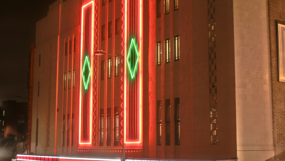 The exterior of art-deco theatre lit up at night.