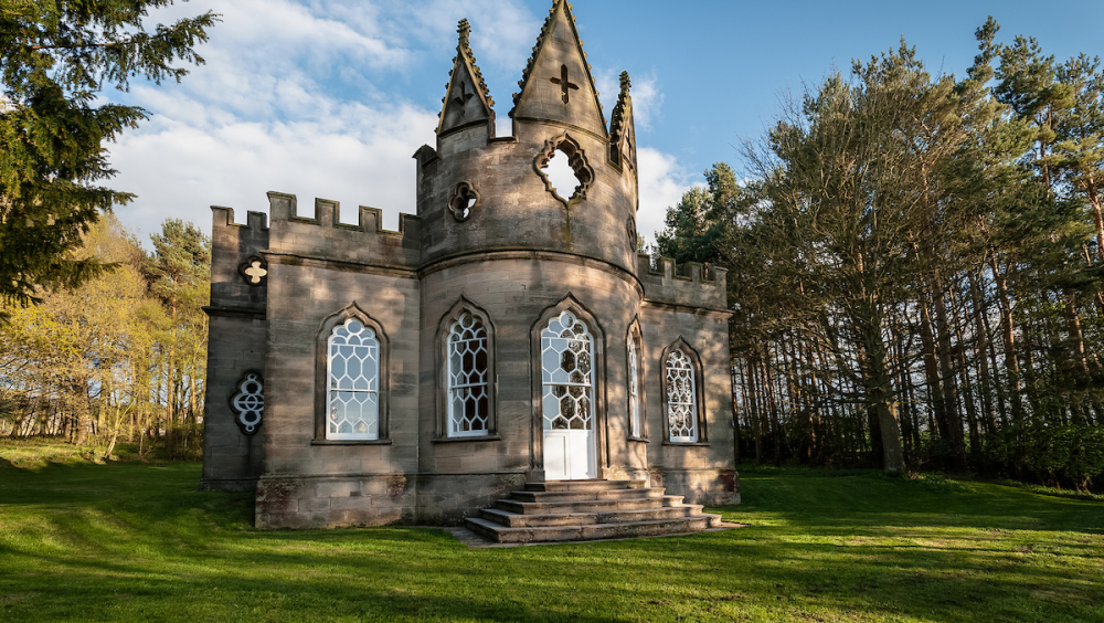 A Gothic-style folly surrounded by trees an grass.