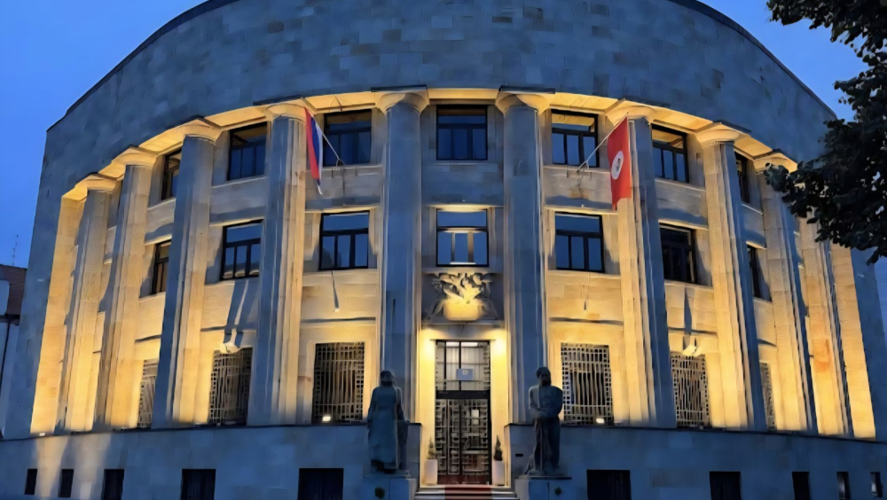 Evening view of the Presidency Building in Banja Luka, a monumental structure with columns, flags, and a central entrance, located on a city square.