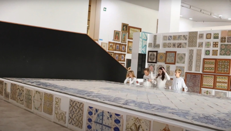 "Four young participants in the Heritage Makers contest explore a tiled exhibit showcasing intricate and colorful patterns, surrounded by framed cultural artifacts in a museum setting."