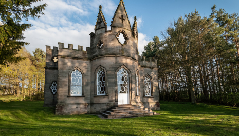A Gothic-style folly surrounded by trees an grass.