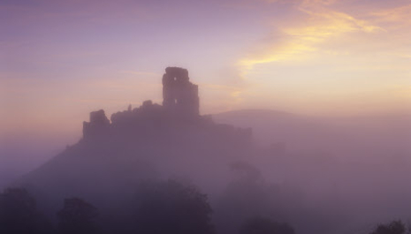 A misty silhouetted Corfe Castle with a purple sky behind.