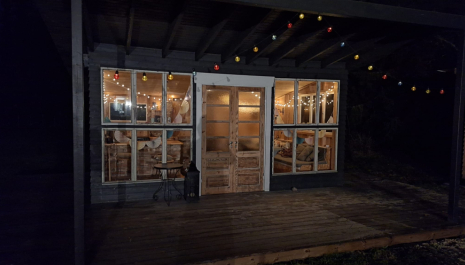 Photograph of a small building. It is dark outside, but the cabin is warmly lit and looks inviting. 